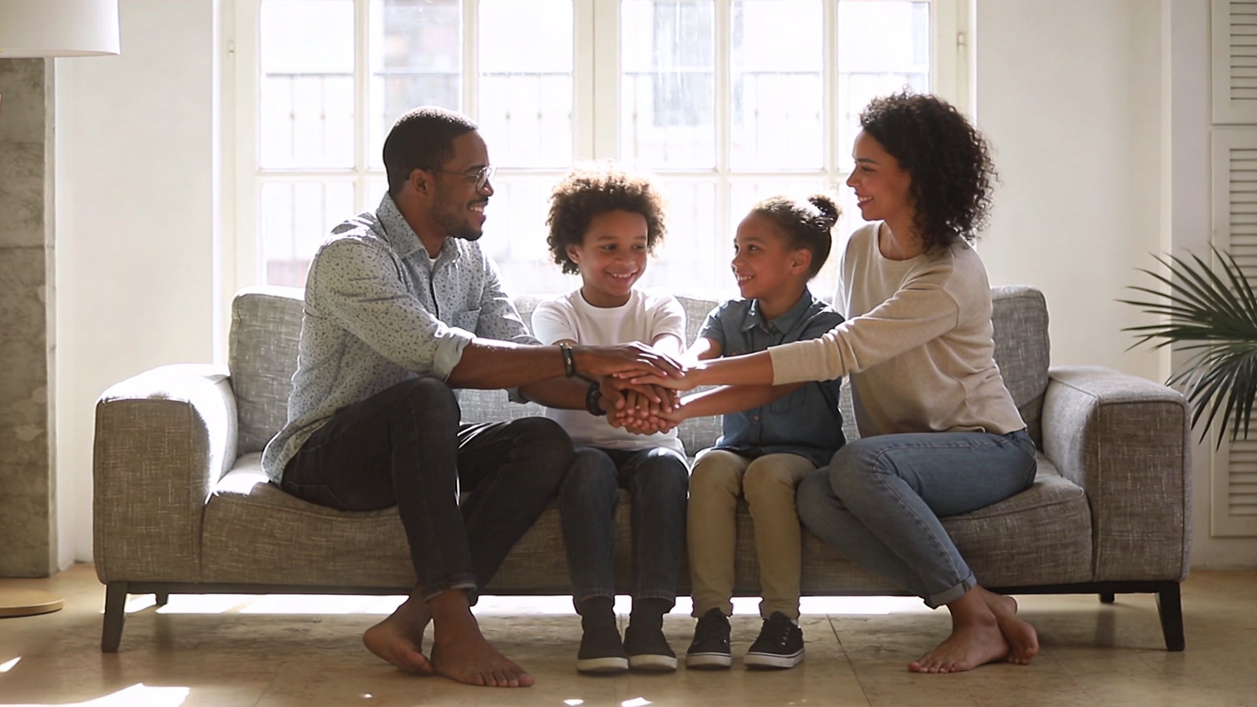 A happy multi-generational family sitting on a sofa with their hands stacked together in unity.