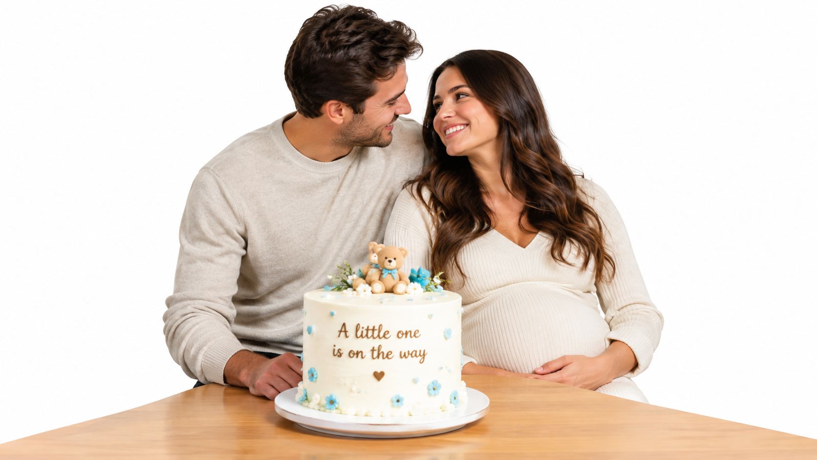 A happy expectant couple smiling at each other behind a celebratory cake announcing their pregnancy